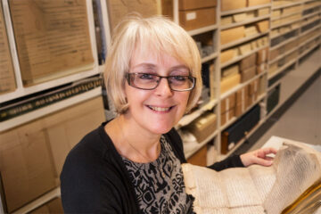 Rachel Hart sits in an archive room holding a parchment